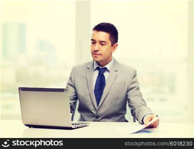 business, people, paperwork and technology concept - businessman with laptop computer and papers working in office