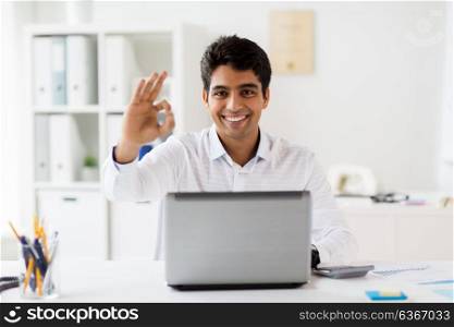 business, people, paperwork and technology concept - businessman with laptop computer showing ok hand sign at office. businessman with laptop showing ok sign at office