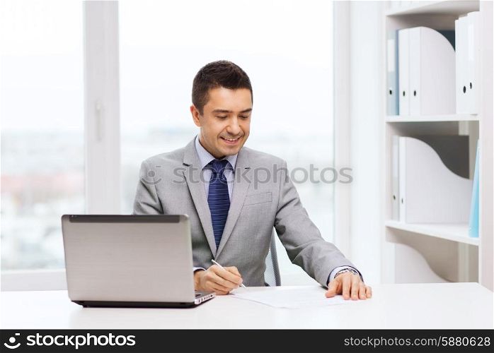 business, people, paperwork and technology concept - smiling businessman with laptop computer and papers working in office