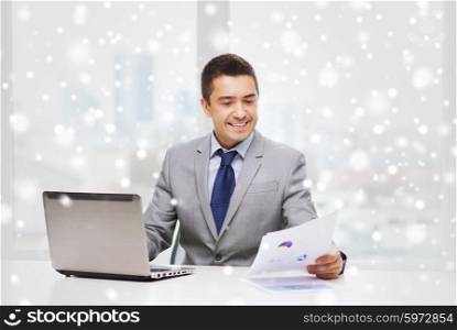 business, people, paperwork and technology concept - smiling businessman with laptop computer and papers working in office over snow effect