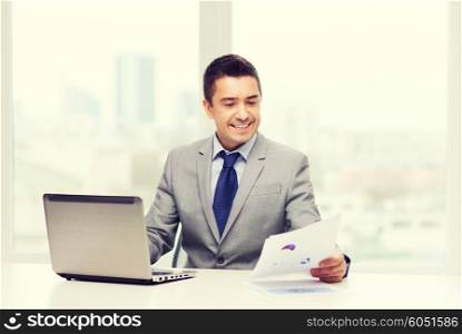 business, people, paperwork and technology concept - smiling businessman with laptop computer and papers working in office