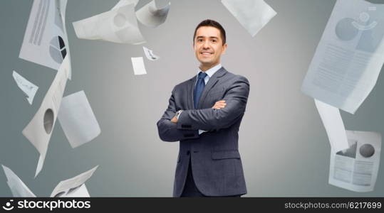 business, people, paperwork, statistics and office concept - happy smiling businessman in dark grey suit over gray background with falling papers