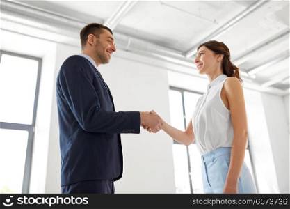 business people, partnership and cooperation concept - happy smiling businesswoman and businessman shaking hands at office. businesswoman and businessman shaking hands