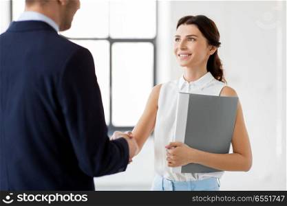 business people, partnership and cooperation concept - happy smiling businesswoman with folder and businessman shake hands at office. businesswoman and businessman shake hands. businesswoman and businessman shake hands