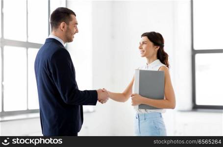business people, partnership and cooperation concept - happy smiling businesswoman with folder and businessman shake hands at office. businesswoman and businessman shake hands