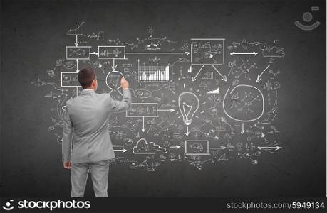 business, people, planning and strategy concept - businessman writing or drawing business scheme over dark gray concrete wall background