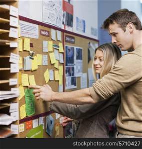 Business people reading reminders on bulletin board in office