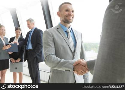 Business people shaking hands and smiling, finishing up a meeting in office. Happy business people shaking hands