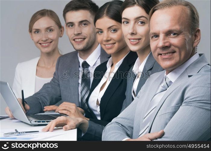Business people sitting in a row. Smiling business people sitting in a row and working at the table with laptop