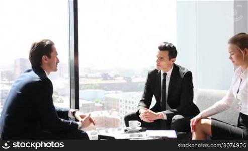 Business people sitting near panoramic window with view on city and talking
