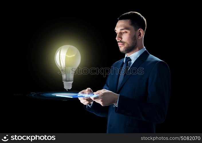 business, people, startup idea, inspiration and modern technology concept - businessman in suit working with transparent tablet pc computer and lightbulb over black background. businessman with tablet pc and lightbulb