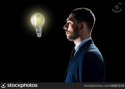 business, people, startup idea, inspiration and technology concept - businessman in suit looking at lightbulb over black background. businessman looking at lightbulb over black
