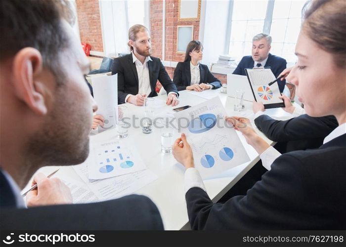 Business, people, statistics and team work concept - creative team with charts on paper, smartphones and tablet pc computers sitting at table in office. Business team with charts