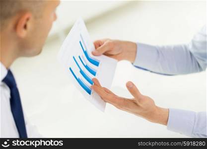 business, people, statistics and teamwork concept - close up of businessman hands showing chart to other man at office