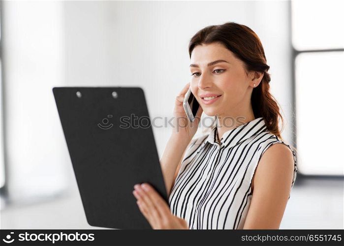 business people, technology and corporate concept - businesswoman or realtor with clipboard calling on smartphone at office. businesswoman calling on smartphone at office. businesswoman calling on smartphone at office