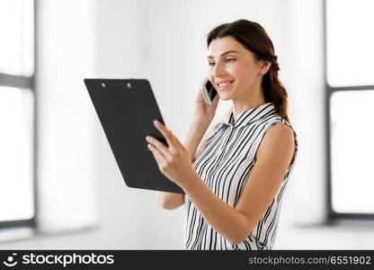 business people, technology and corporate concept - businesswoman or realtor with clipboard calling on smartphone at office. businesswoman calling on smartphone at office. businesswoman calling on smartphone at office