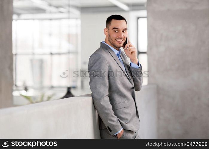 business people, technology and corporate concept - happy smiling businessman calling on smartphone at office. businessman calling on smartphone at office. businessman calling on smartphone at office