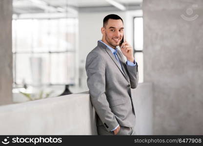 business people, technology and corporate concept - happy smiling businessman calling on smartphone at office. businessman calling on smartphone at office. businessman calling on smartphone at office