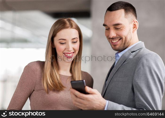 business people, technology and corporate concept - happy smiling businesswoman and businessman with smartphone at office. businesswoman and businessman with smartphone