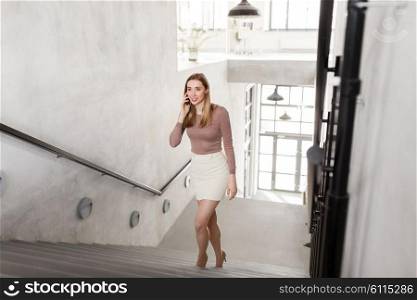 business people, technology and corporate concept - happy smiling businesswoman calling on smartphone and walking upstairs at office. businesswoman with smartphone walking upstairs. businesswoman with smartphone walking upstairs