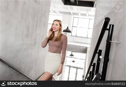 business people, technology and corporate concept - happy smiling businesswoman calling on smartphone and walking upstairs at office. businesswoman with smartphone walking upstairs