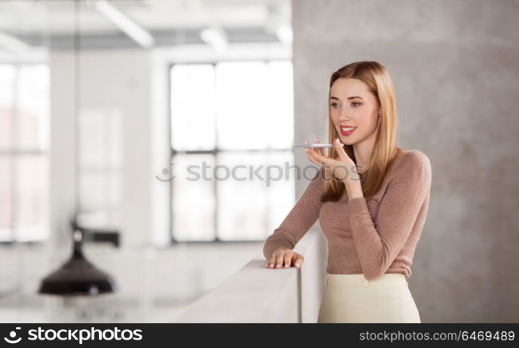 business people, technology and corporate concept - happy smiling businesswoman using voice command recorder on smartphone at office. woman using voice recorder on smartphone at office