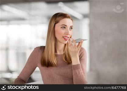 business people, technology and corporate concept - happy smiling businesswoman using voice command recorder on smartphone at office. woman using voice recorder on smartphone at office. woman using voice recorder on smartphone at office