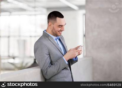 business people, technology and corporate concept - smiling businessman with smarphone at office. smiling businessman with smarphone at office