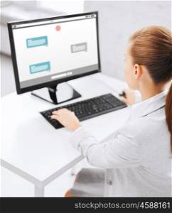 business, people, technology and education concept - businesswoman or student girl with messenger on computer screen sitting at office table
