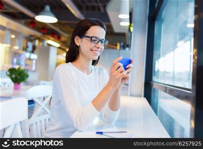 business, people, technology and lifestyle concept - smiling young woman in eyeglasses texting message with smartphone at cafe
