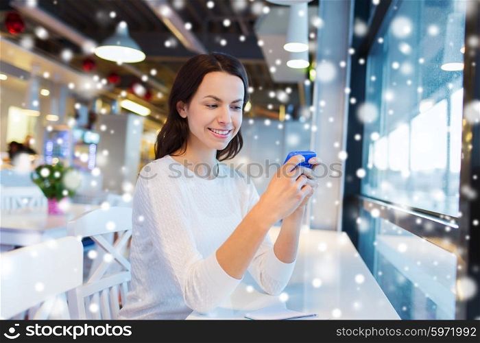 business, people, technology and lifestyle concept - smiling young woman texting message with smartphone at cafe over snow effect