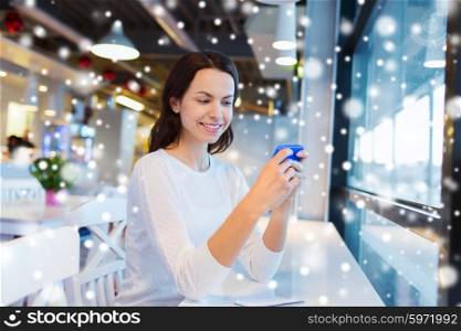 business, people, technology and lifestyle concept - smiling young woman texting message with smartphone at cafe over snow effect