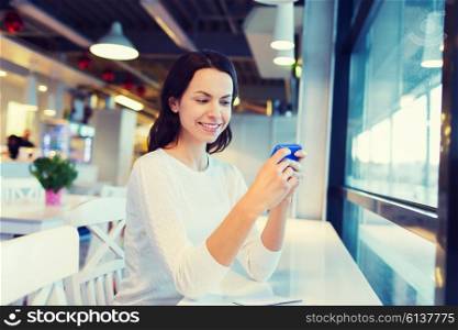 business, people, technology and lifestyle concept - smiling young woman texting message with smartphone at cafe