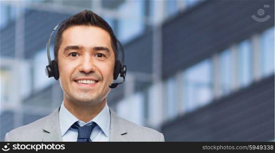 business, people, technology and service concept - smiling businessman in headset over city office building background