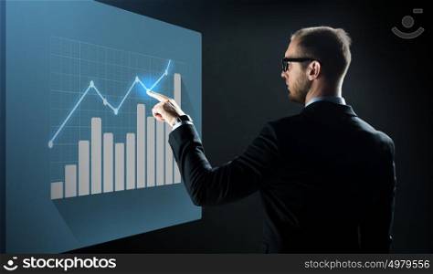 business, people, technology and statistics concept - businessman in suit and glasses pointing finger to virtual screen with diagram chart over black background. businessman pointing finger to virtual chart