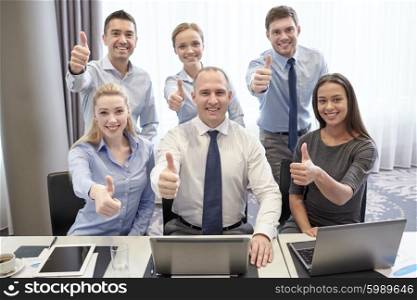business, people, technology, gesture and teamwork concept - smiling business team with laptop computers showing thumbs up in office