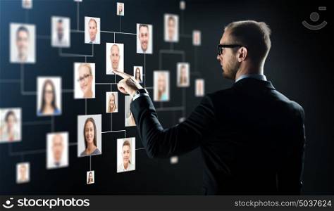 business, people, technology, hiring and employment concept - businessman in suit and glasses pointing finger to contact icons over black background. businessman pointing finger to