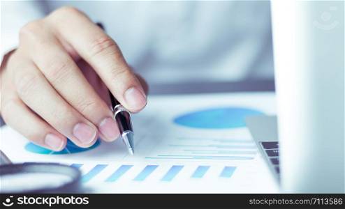 Business people use pen to point graphs to analyze company data and statistics from the chart.