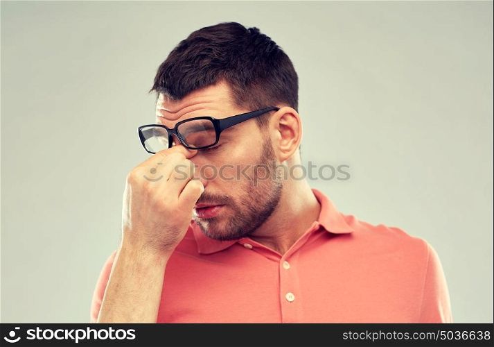business, people, vision and overwork concept - tired man with eyeglasses touching nose bridge over gray background. tired man with eyeglasses touching nose bridge