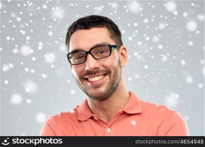 business, people, winter, christmas and eyesight concept - portrait of happy smiling man in eyeglasses over snow on gray background