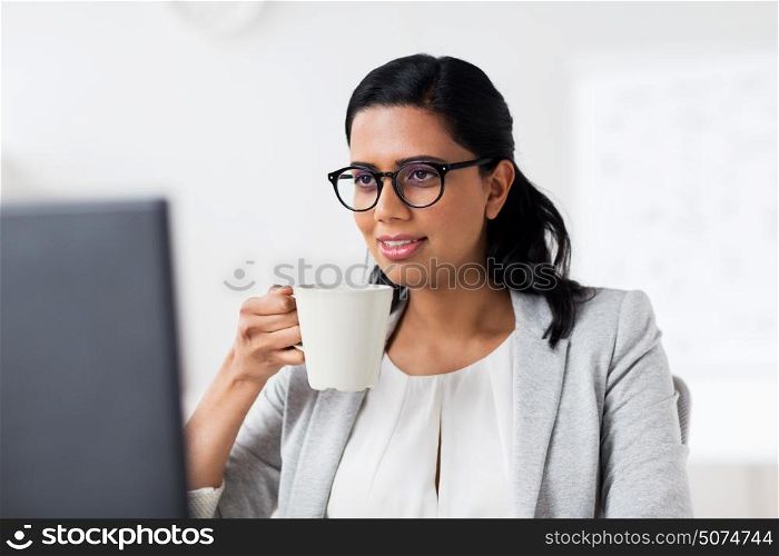 business, people, work and technology concept - happy businesswoman with computer drinking coffee at office. businesswoman drinking coffee at office computer