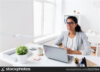 business, people, work and technology concept - happy smiling businesswoman with laptop computer at office. happy smiling businesswoman with laptop at office