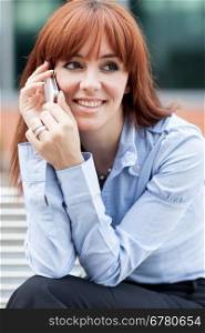 Business photo of red hair businesswoman sitting on a metal bench while phoning