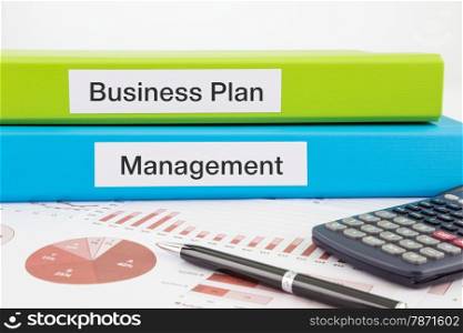 Business Plan and Management words on labels with document binders, graphs and business reports