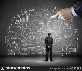 Business planning. Rear view of businessman looking at business sketch on wall