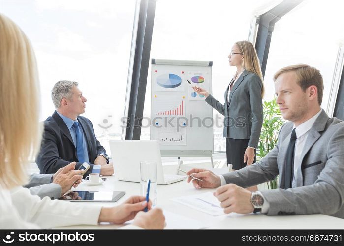 Business presentation of statistics. Business presentation of statistics, business woman pointing at flipchart, team of people at meeting table watching