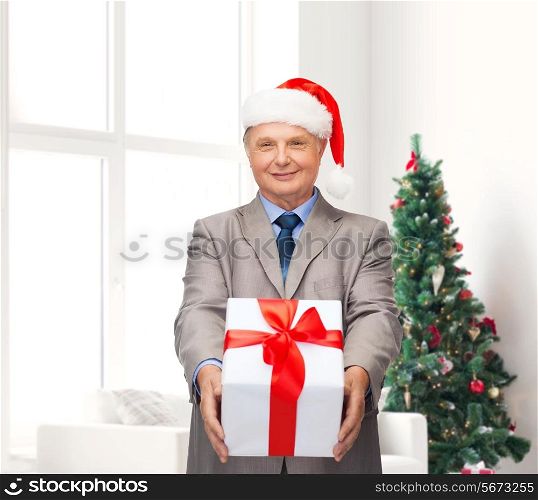 business, presents and people concept - smiling senior man in suit and santa helper hat with gift over living room and christmas tree background