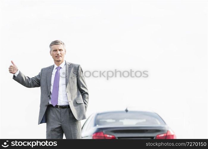 Business professional hitchhiking by breakdown car against sky