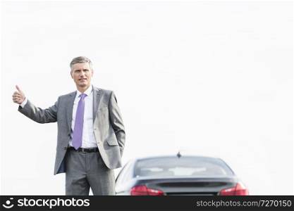 Business professional hitchhiking by breakdown car against sky