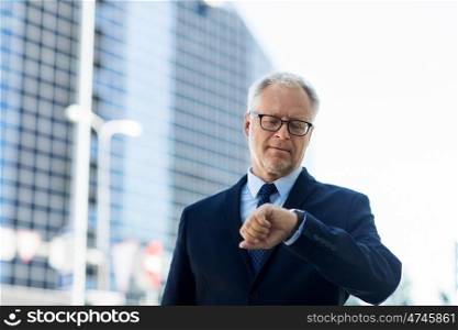 business, punctuality and people concept - senior businessman checking time on wristwatch or smart watch on his hand in city